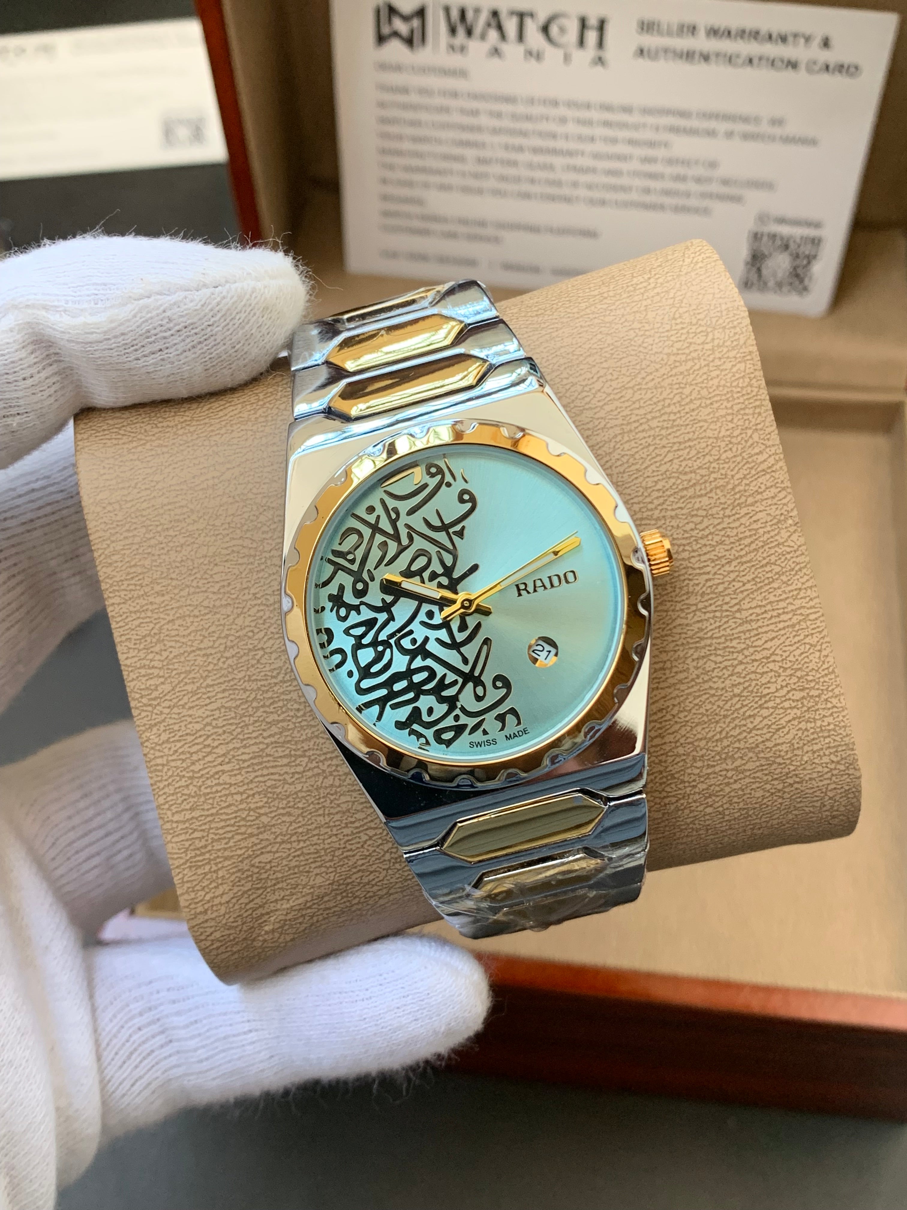 Watch with gold and silver band on a beige cushion, held by a gloved hand.