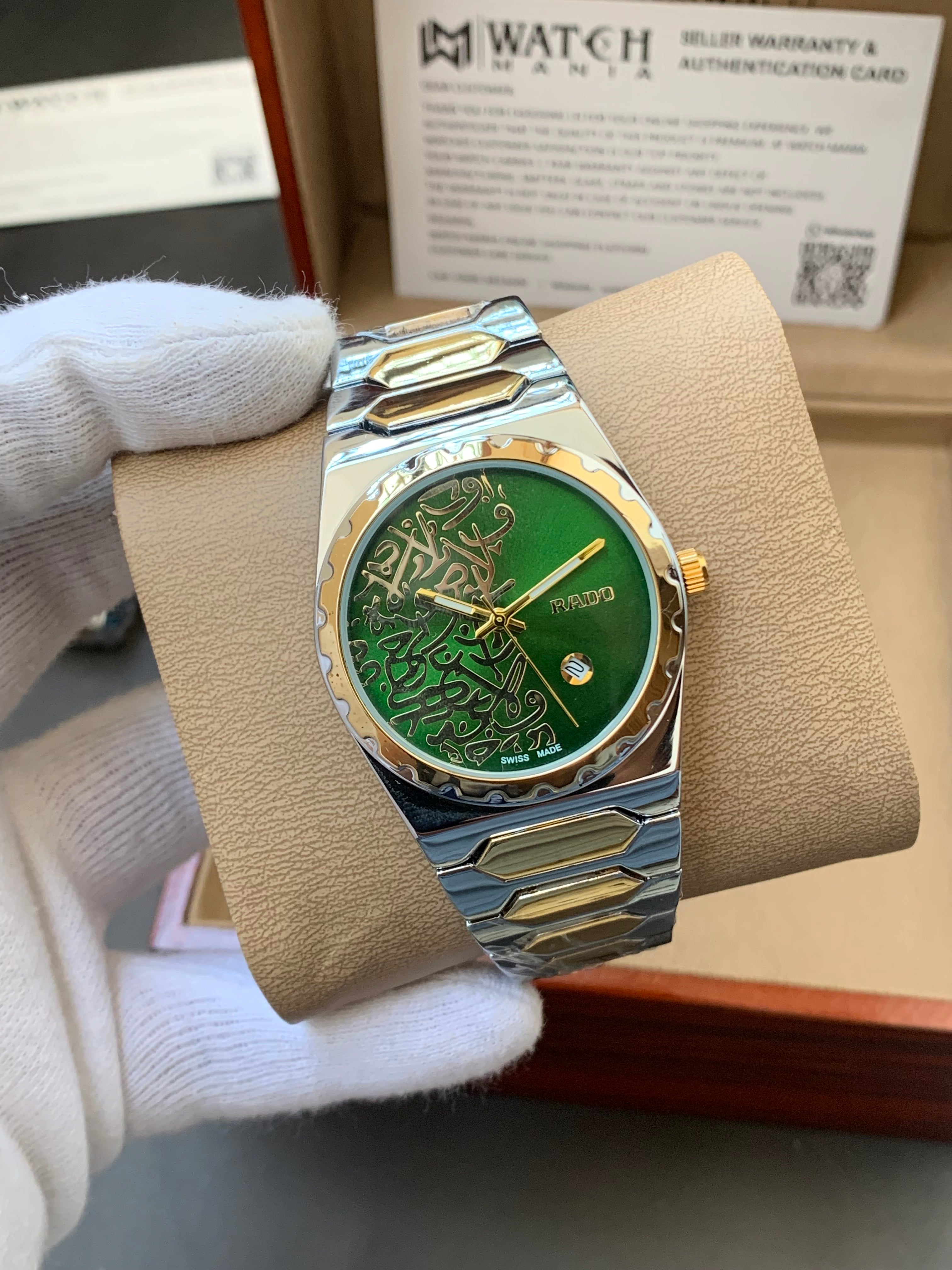 Luxury watch with green face and gold accents on a beige stand, held by a gloved hand.