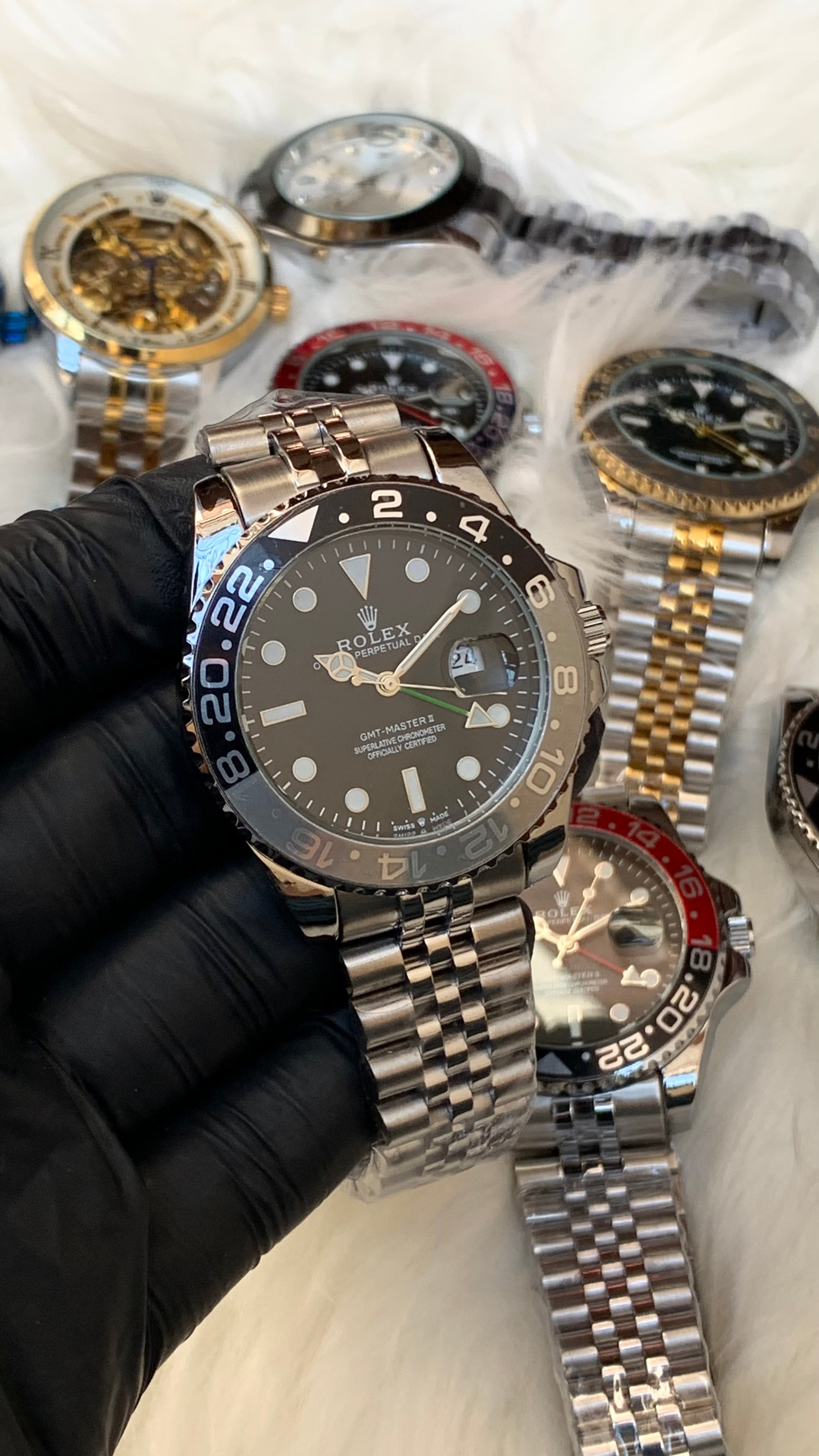 Collection of watches on a white surface with a gloved hand holding one watch.