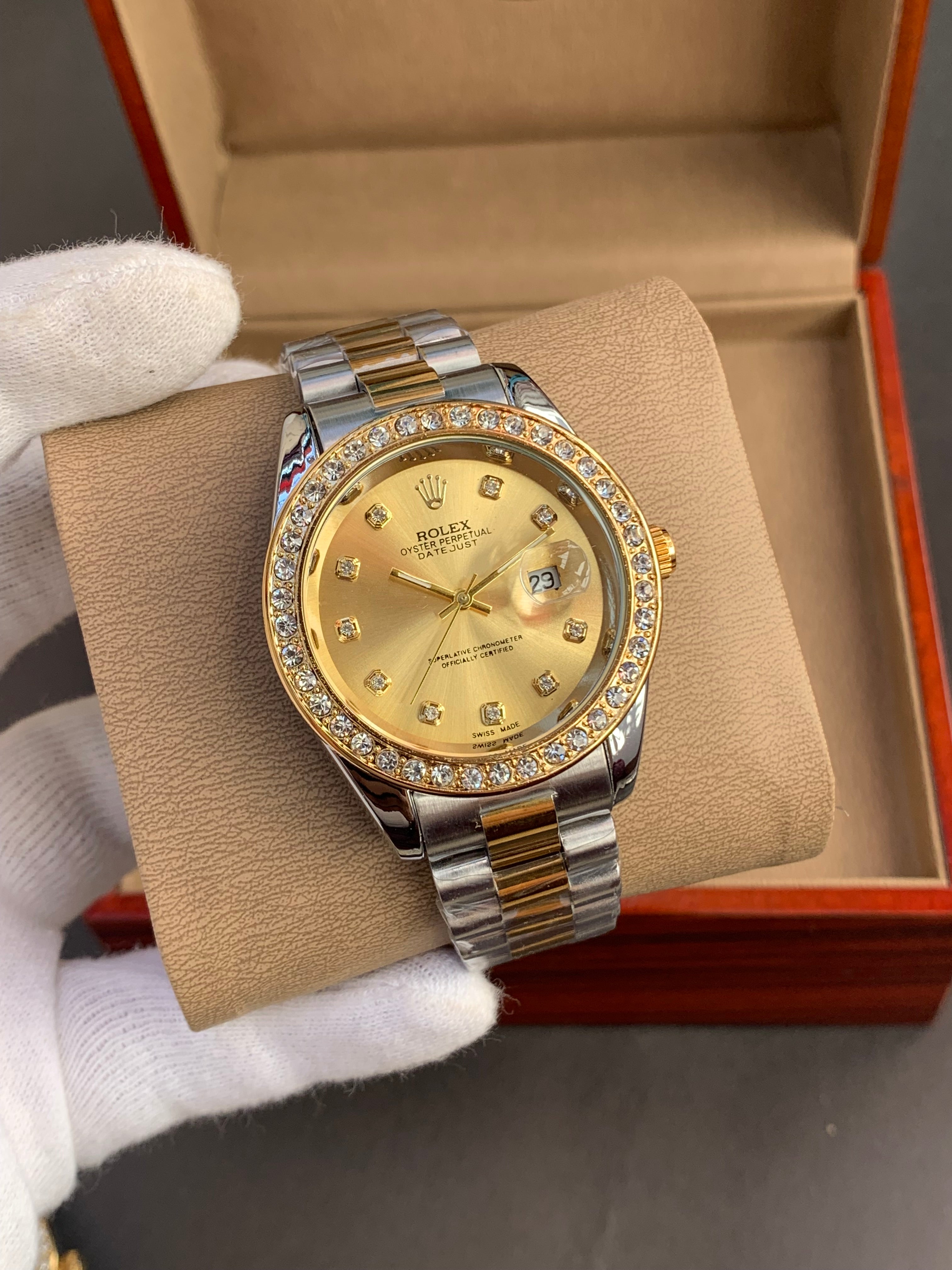 Gold watch with diamond accents on a beige cushion, held by white gloves.