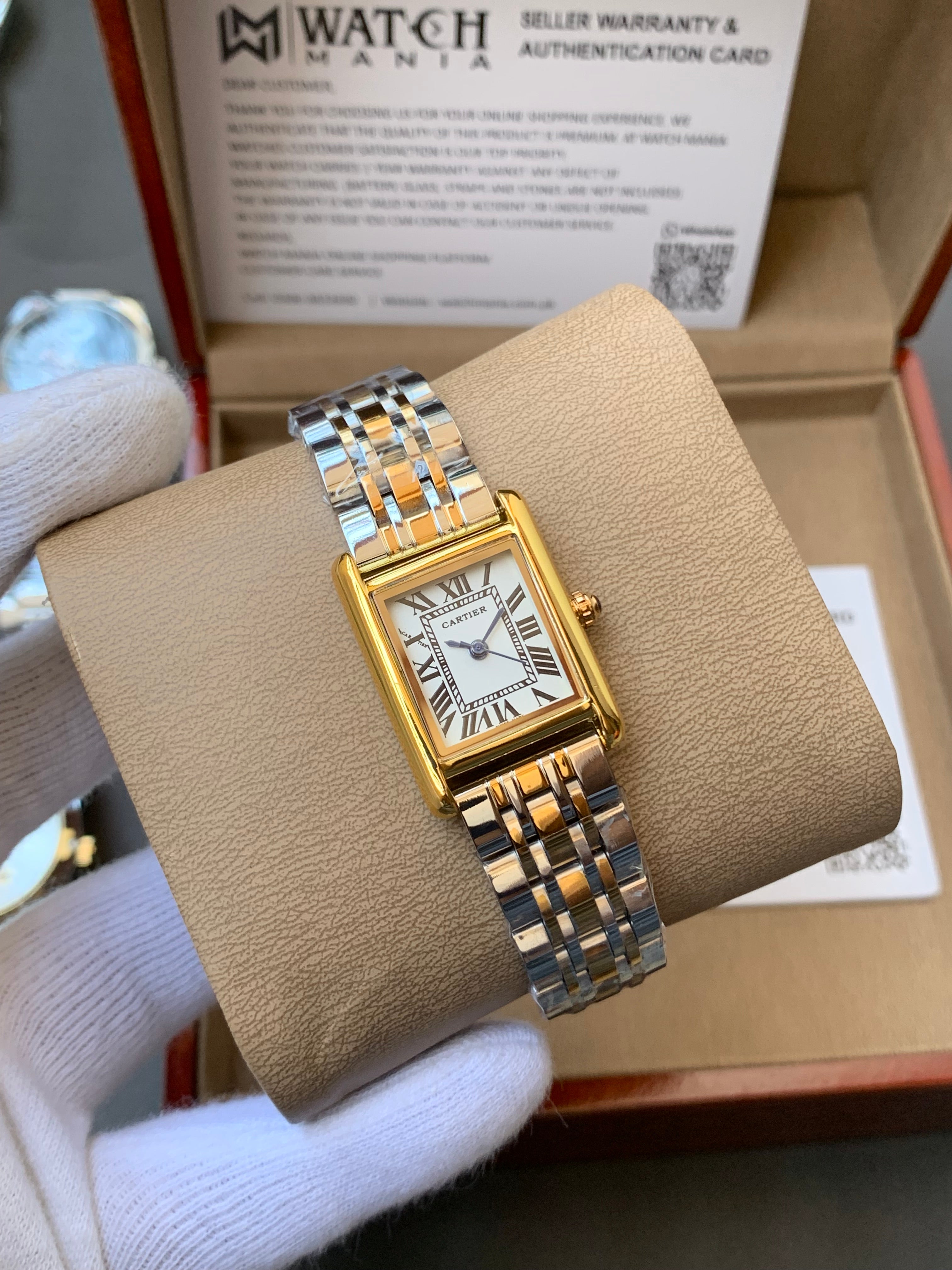 Gold and silver watch on a beige cushion with a box in the background