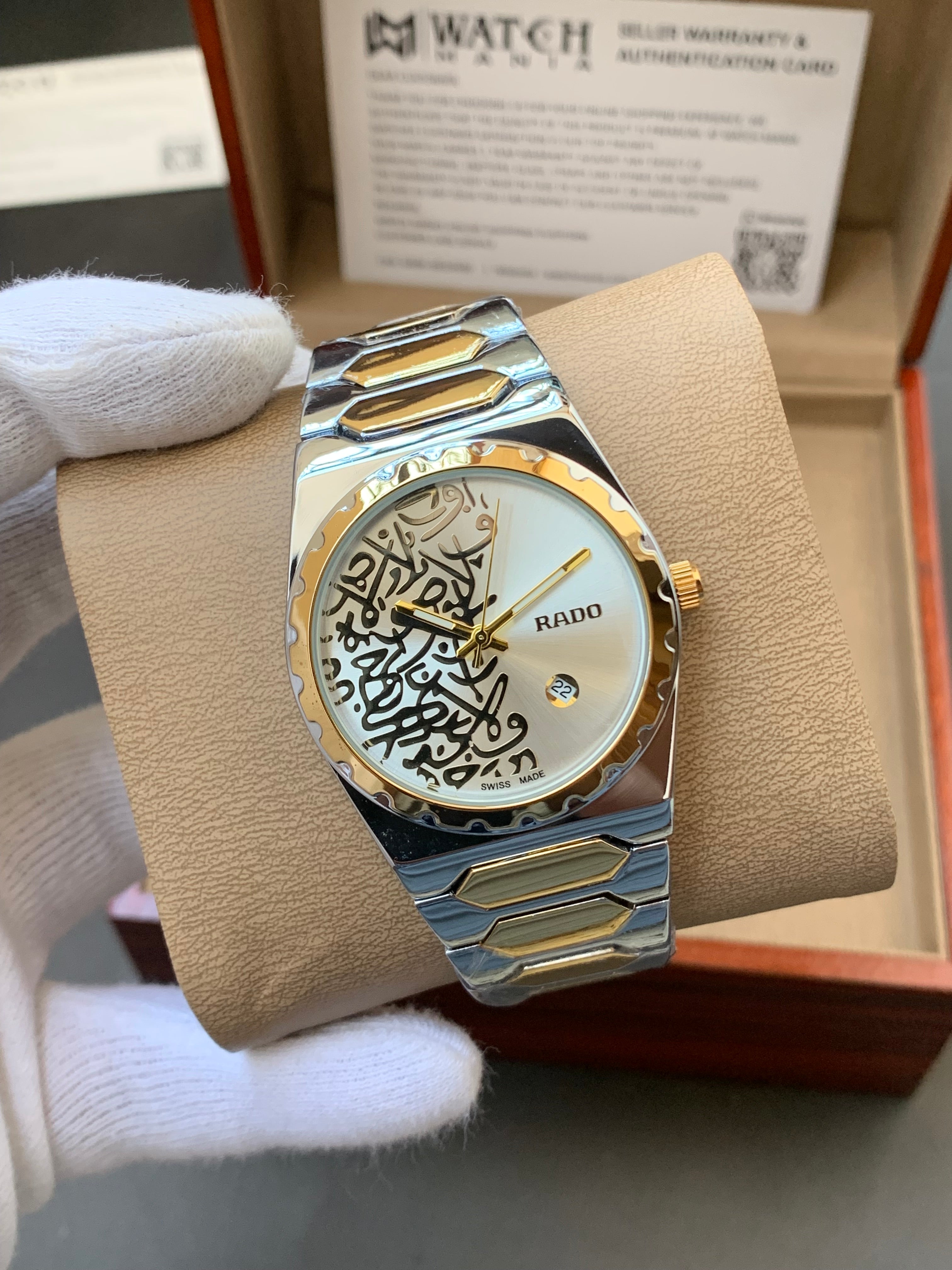 Gold and silver watch with intricate design on a beige cushion, held by a gloved hand.