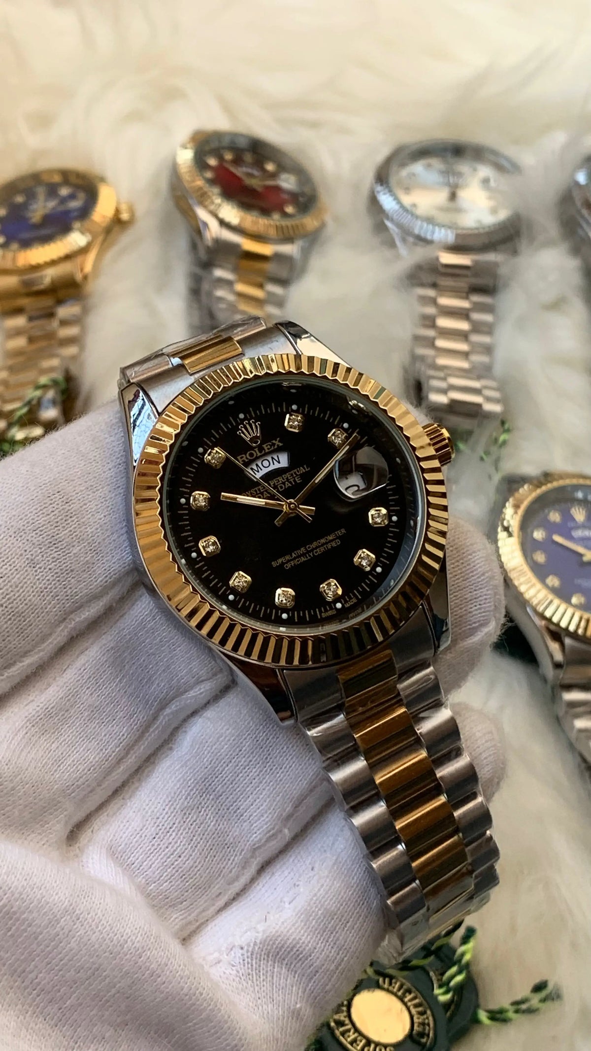Gold and silver watch with black face held by a gloved hand on a white background