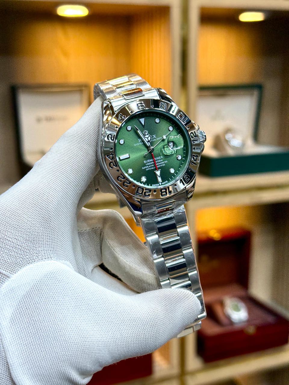 Silver watch with green dial held by a gloved hand, blurred background