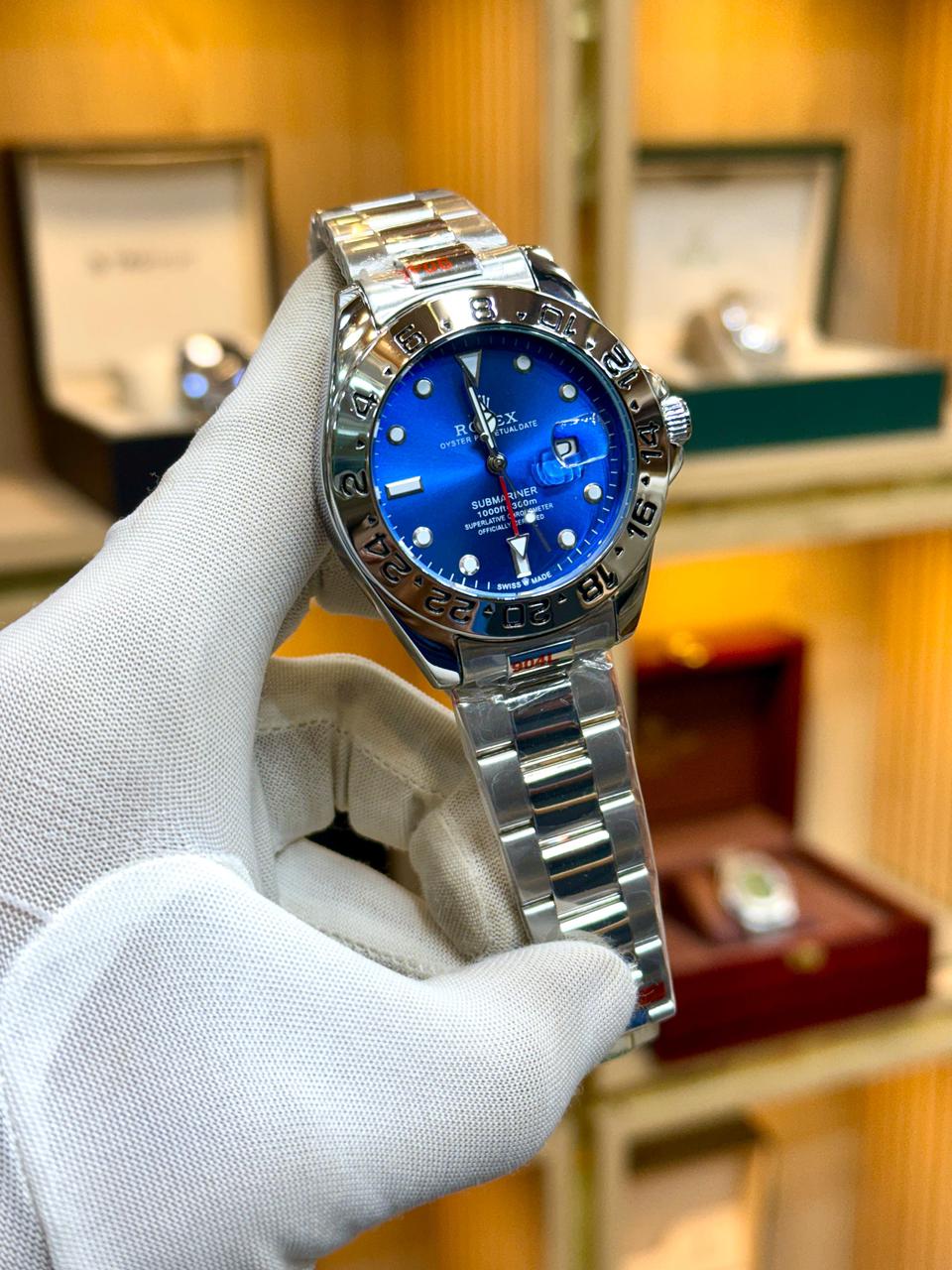 Silver watch with a blue face held by a gloved hand against a blurred background