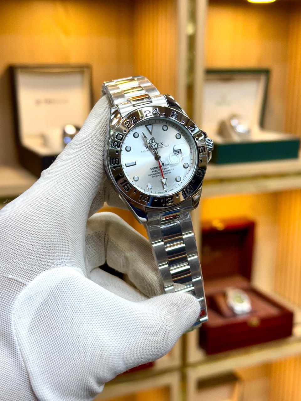Silver watch held by a gloved hand with a blurred background