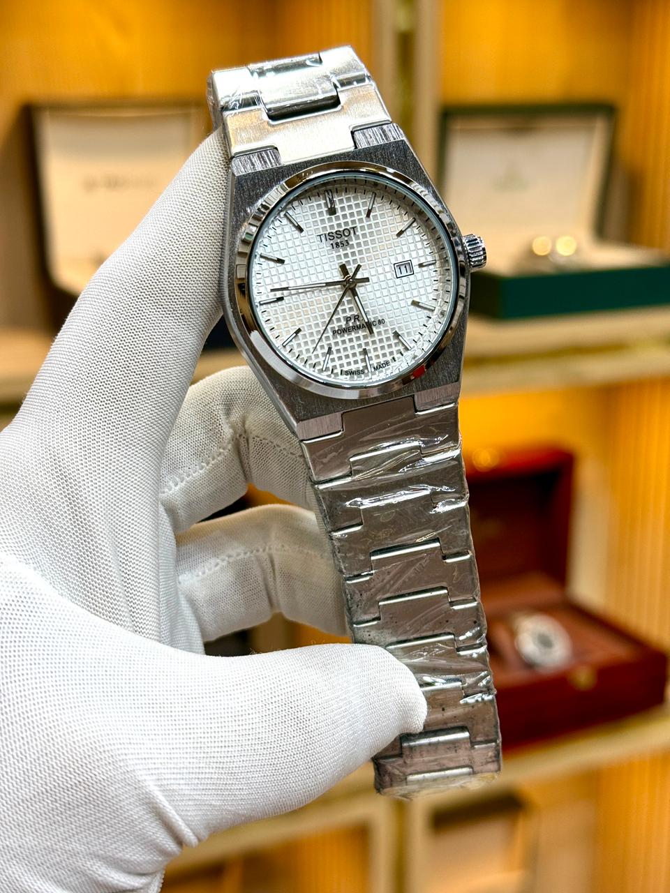 Silver watch held by a gloved hand with a blurred background