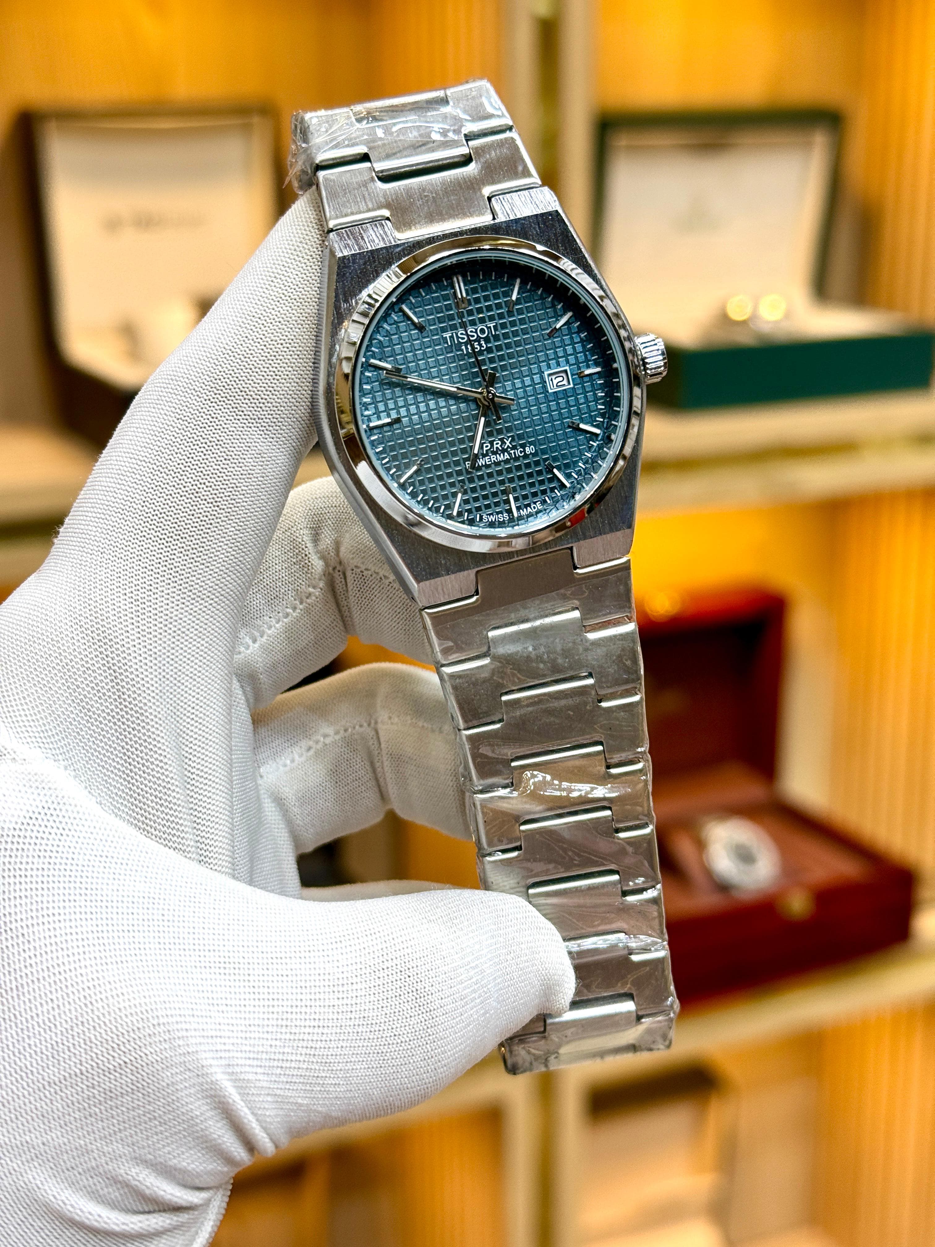 Silver watch with blue face held by a gloved hand against a blurred background