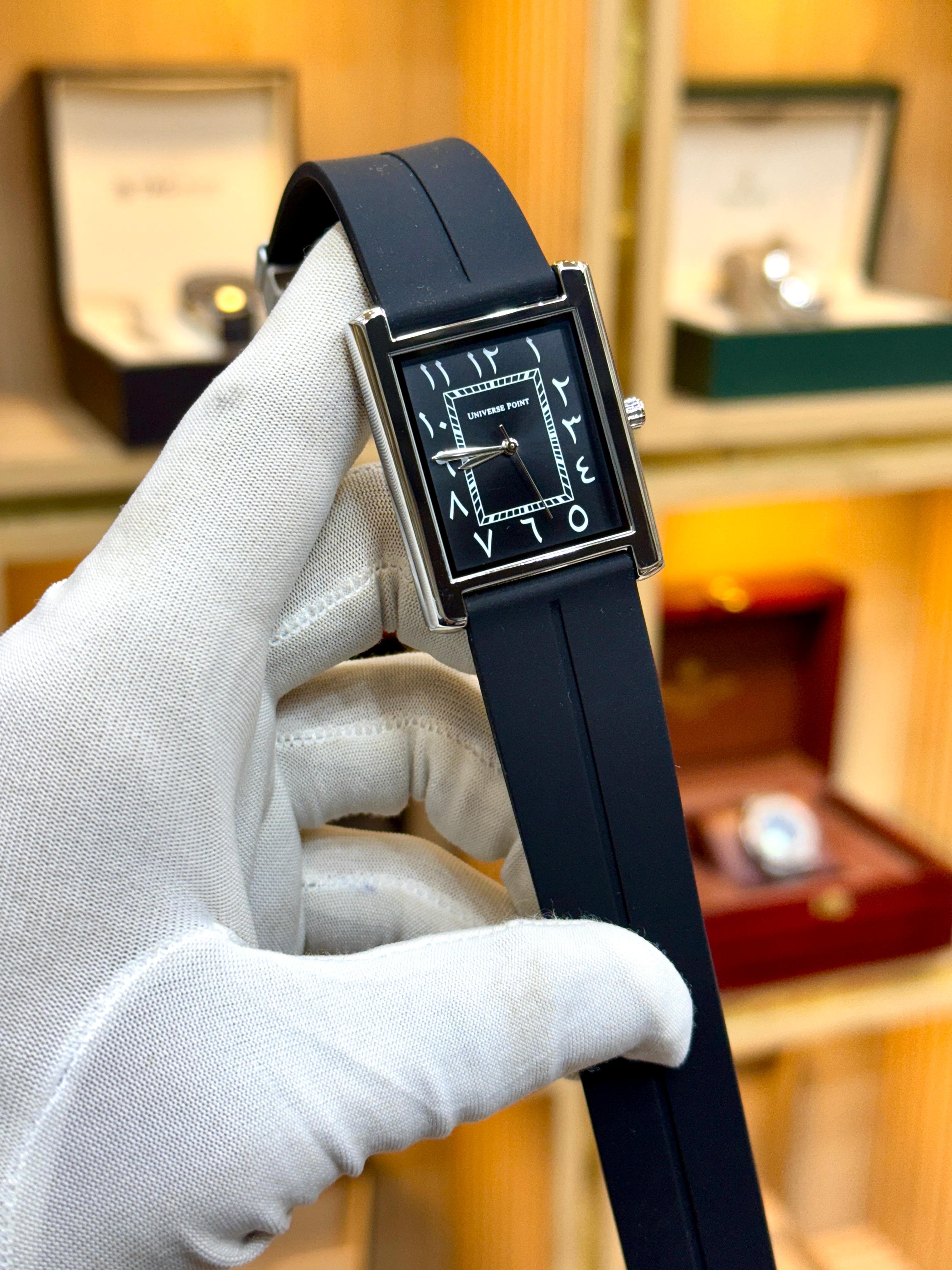 Watch with black strap held by a gloved hand against a blurred background