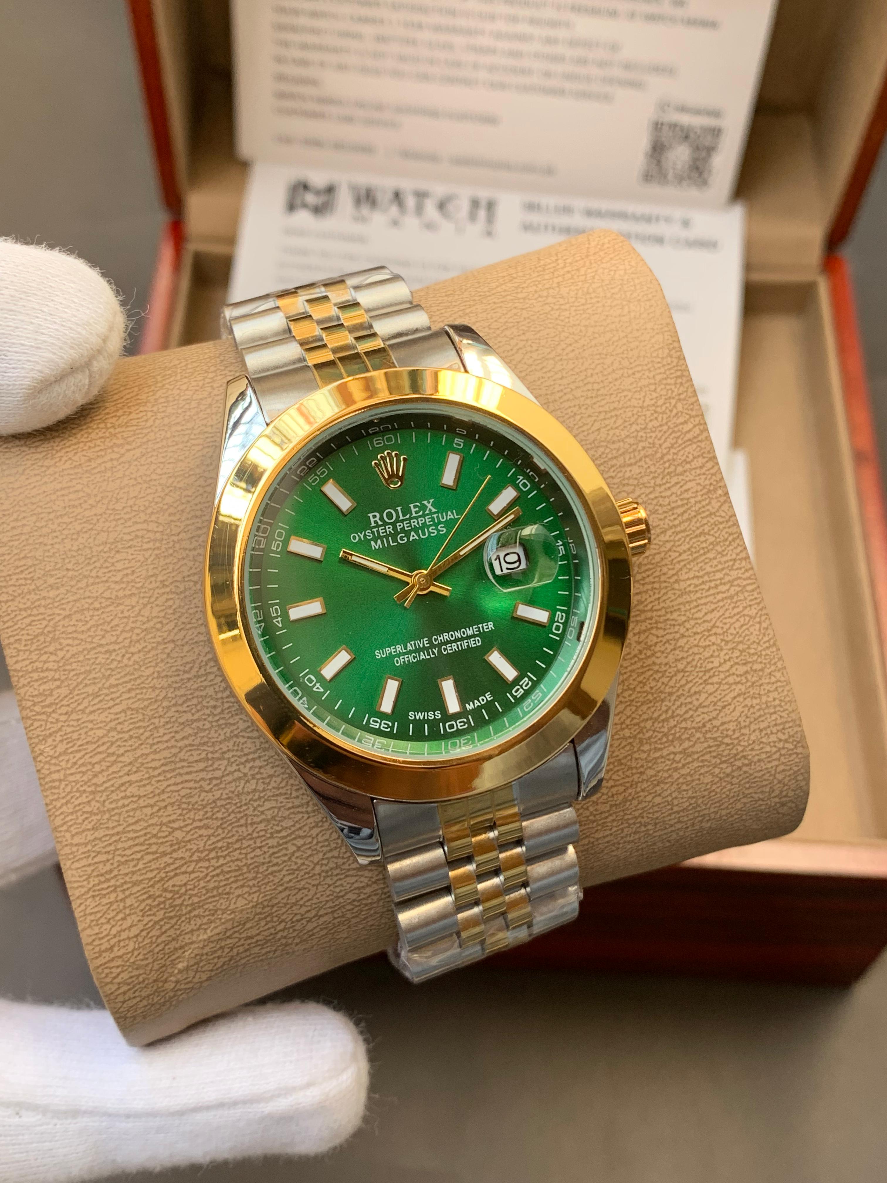 Luxury watch with green face and gold and silver band on a brown cushion