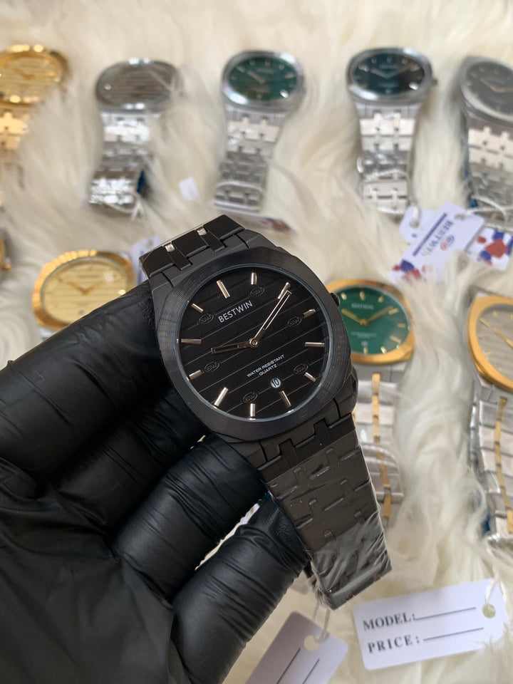 Black wristwatch held by a gloved hand with blurred watches in the background