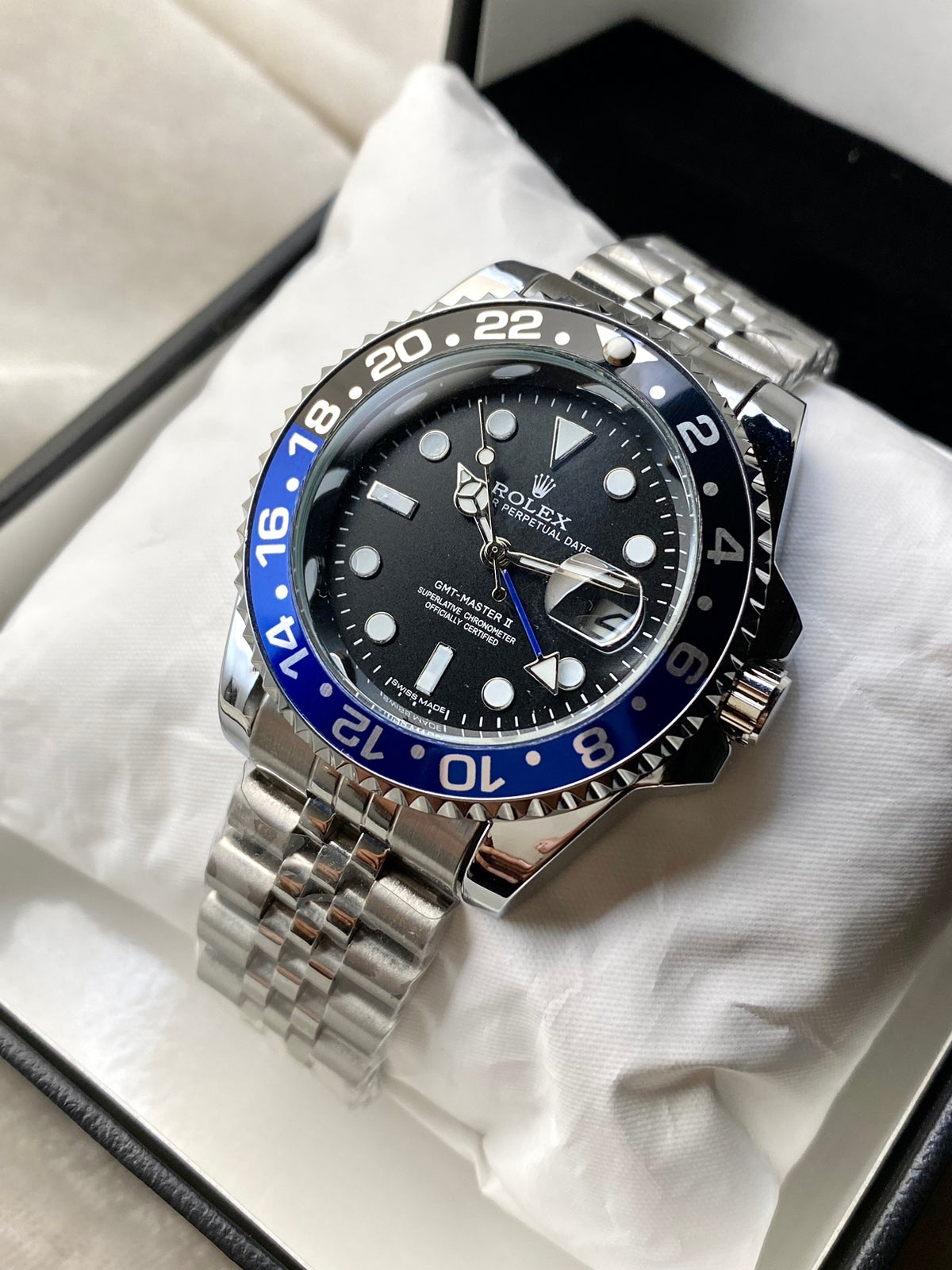 Rolex watch with black face and blue bezel on a white cloth