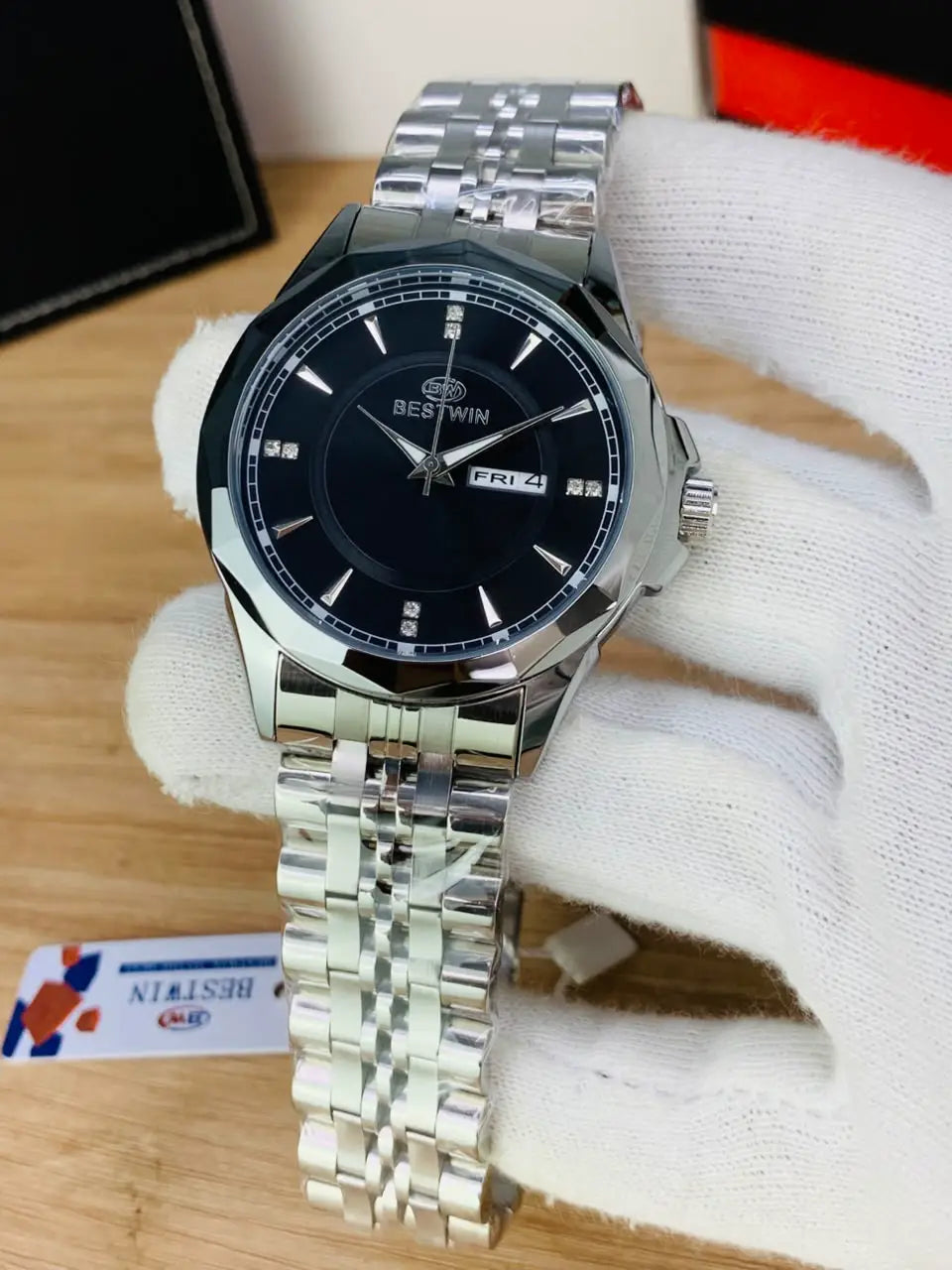 A silver stainless steel wristwatch with a black dial and date window, displayed on a white knit glove over a wooden surface.