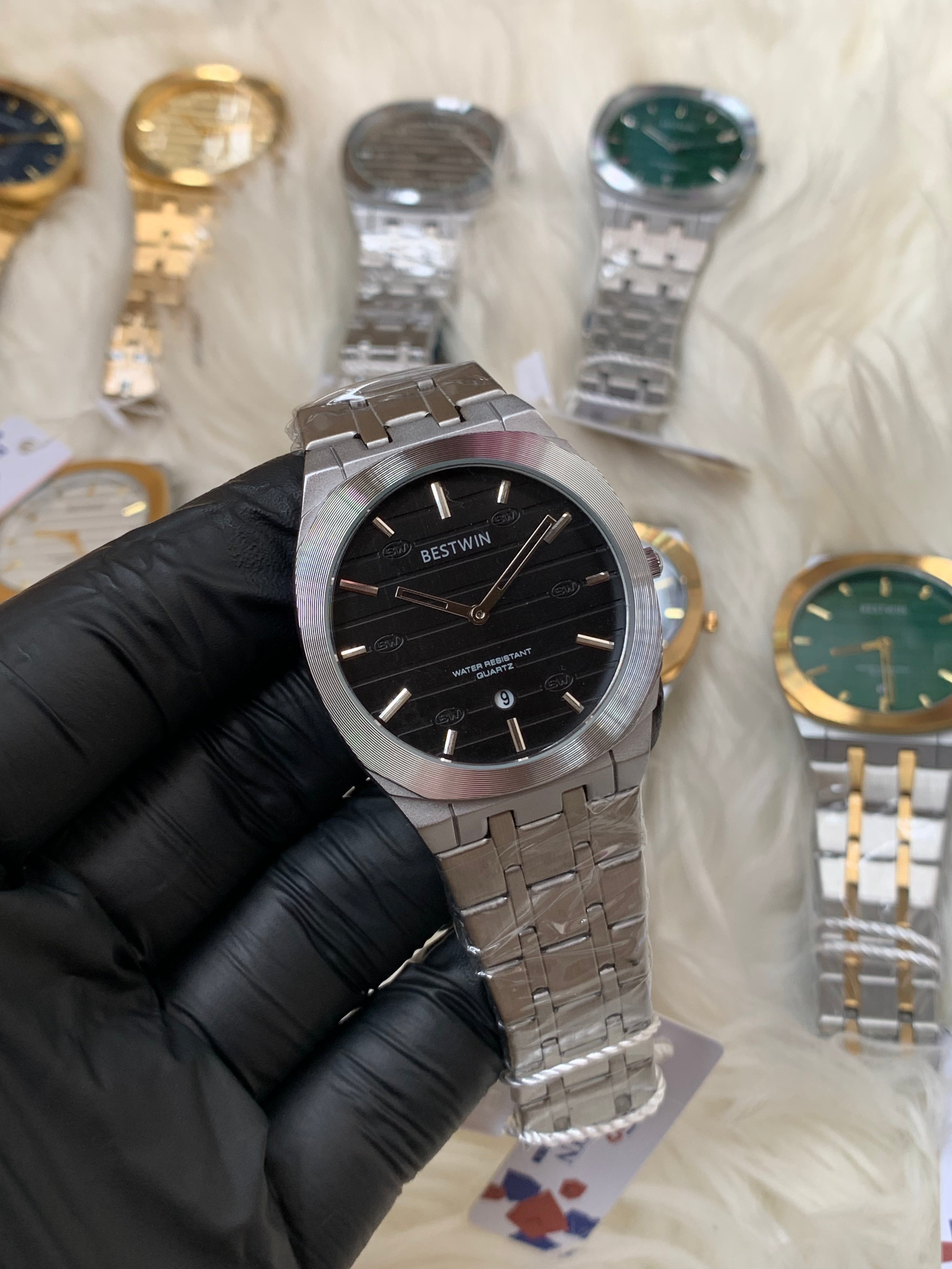 Silver watch held by a gloved hand with other watches in the background