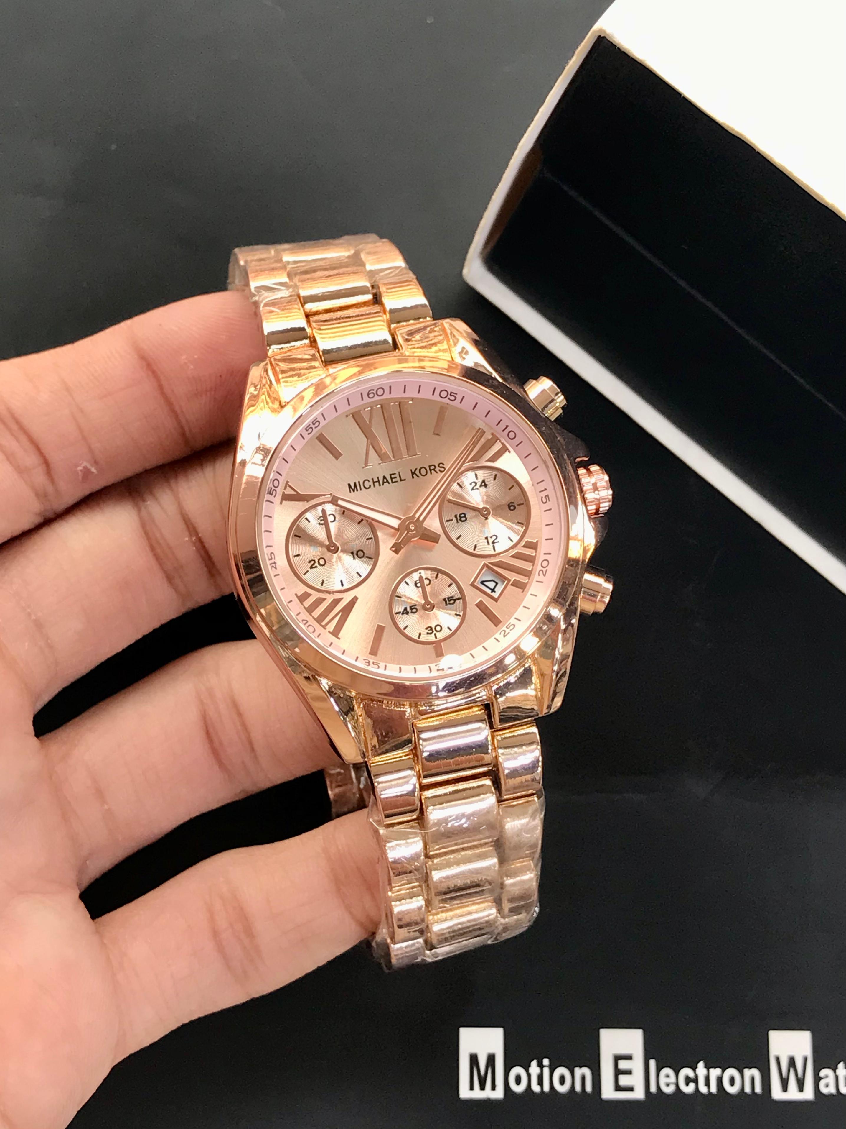 Rose gold watch held by a hand with a black background