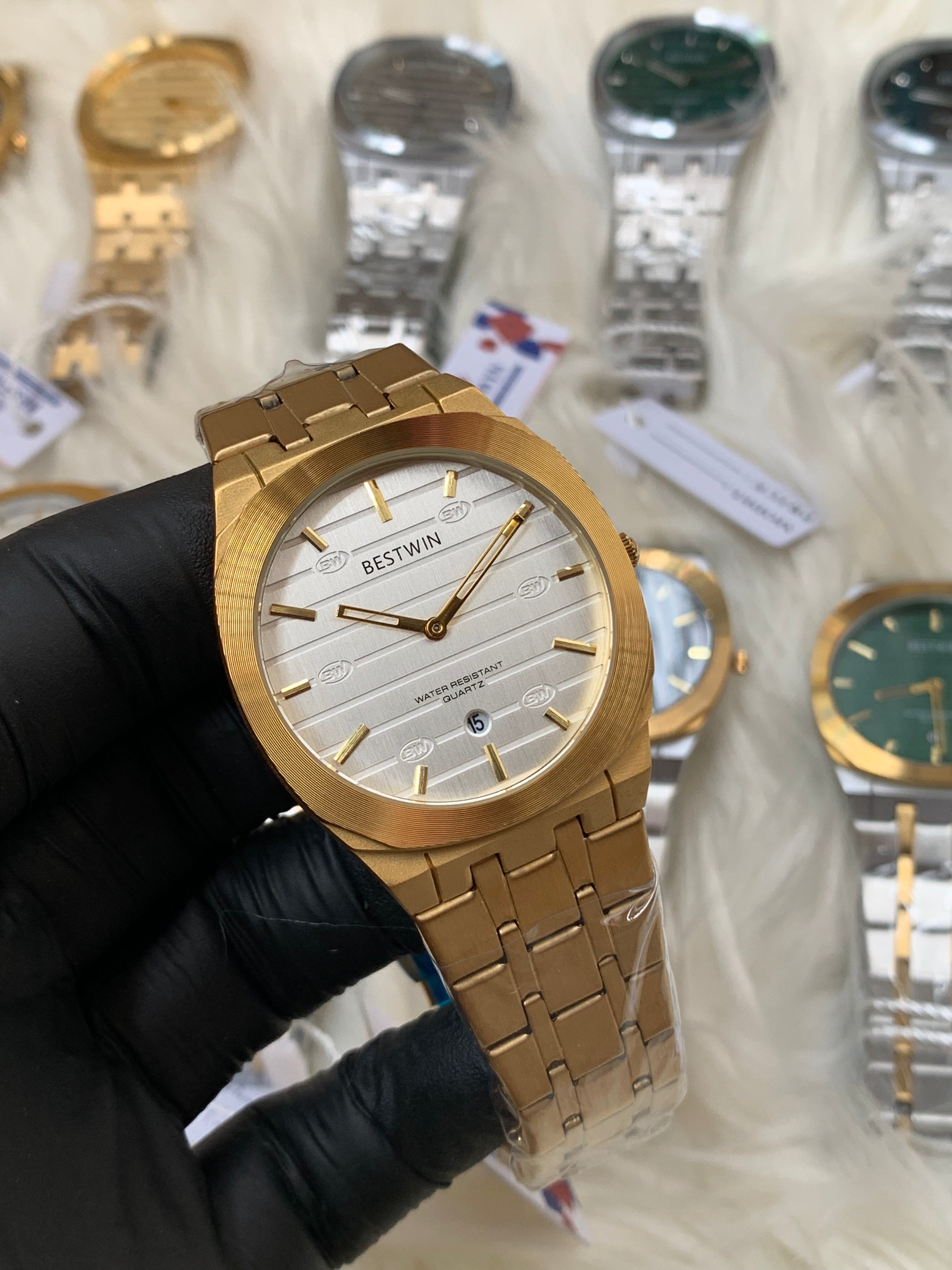 Gold watch held by a gloved hand with other watches in the background