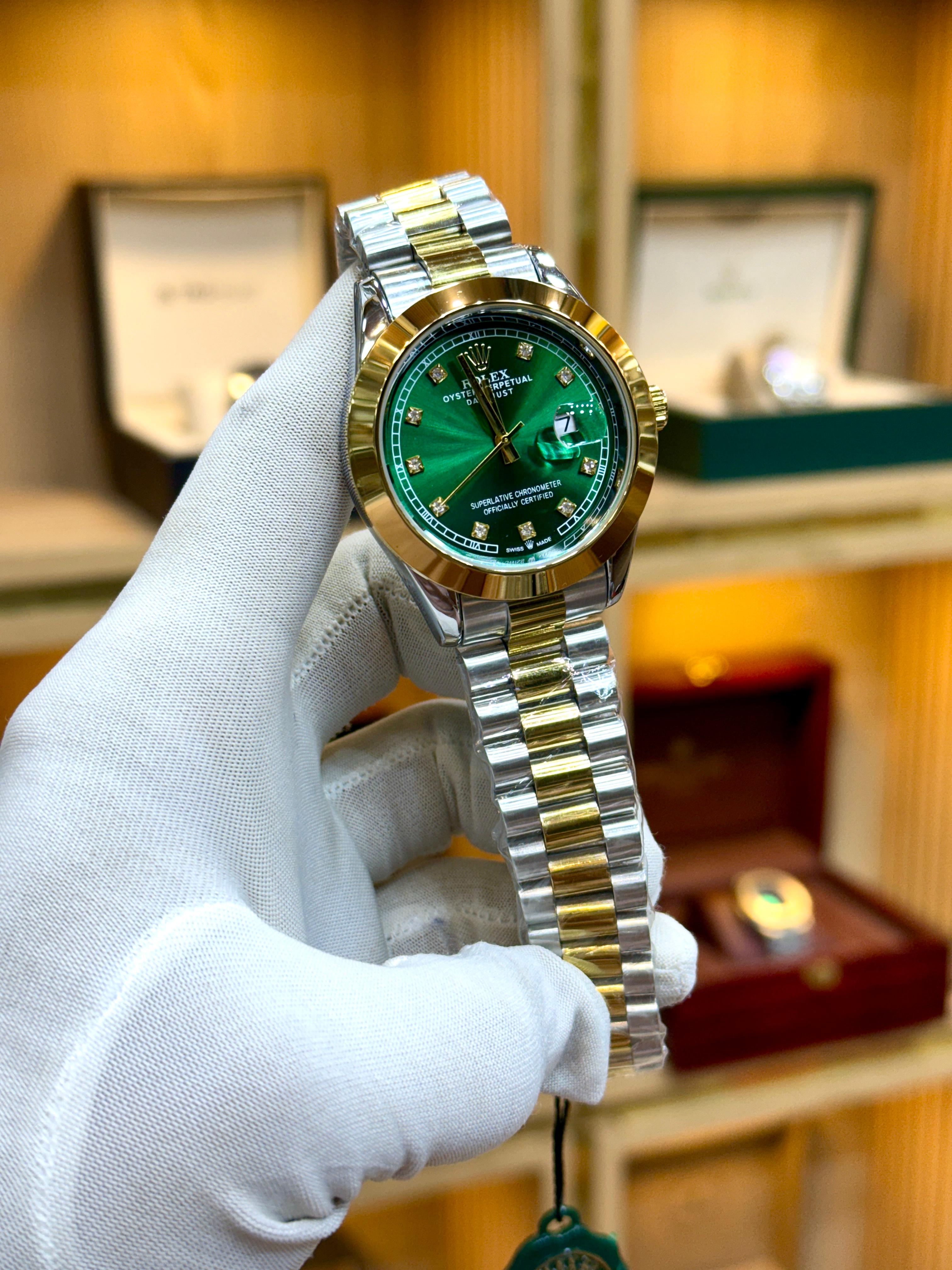 Gold and silver watch with green face held by a gloved hand against a blurred background