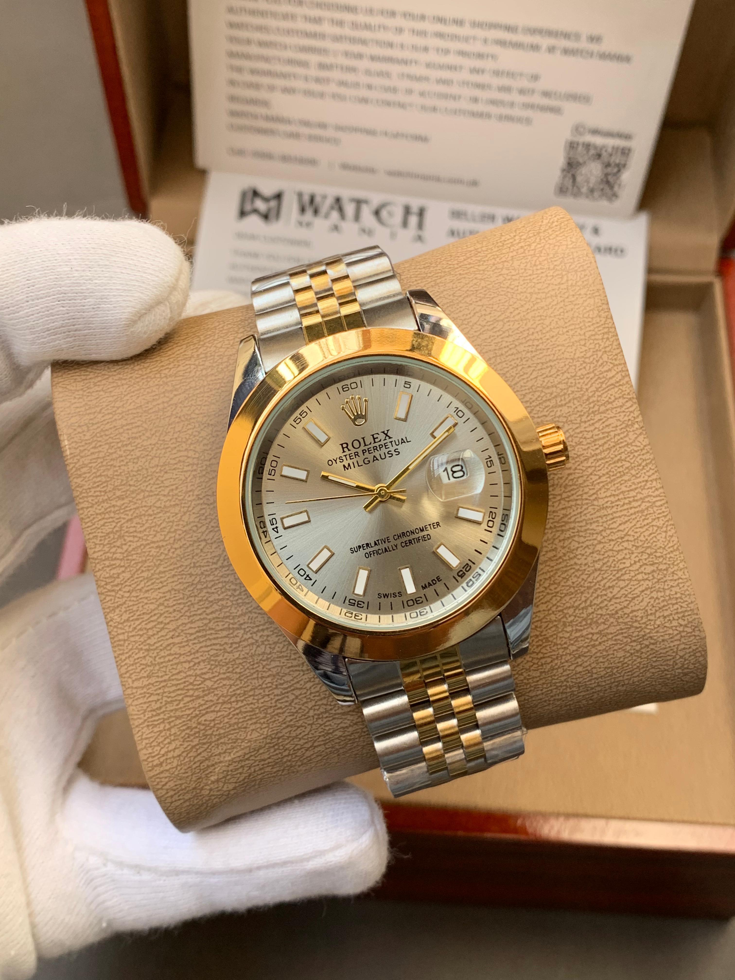 Gold and silver watch on Grey display with a brown cushion, against a blurred background.