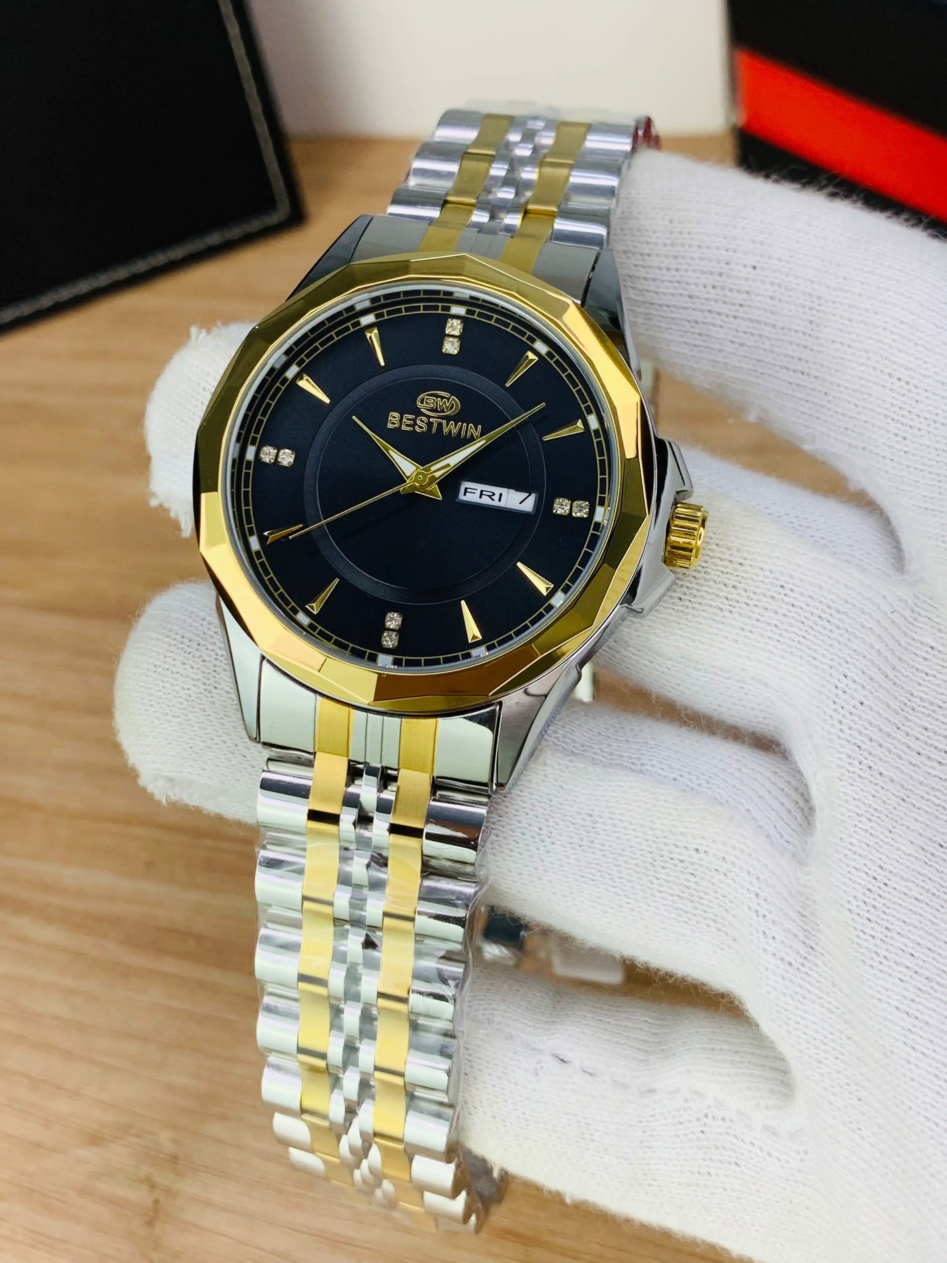 A two-tone stainless steel and gold wristwatch with a black dial, held in a white-gloved hand over a light wood surface.